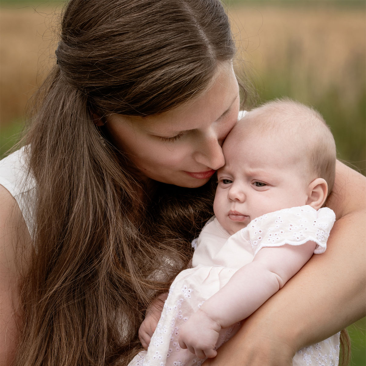 Mama hält ihr Baby liebevoll im Arm und küsst es sanft an der Stirn.